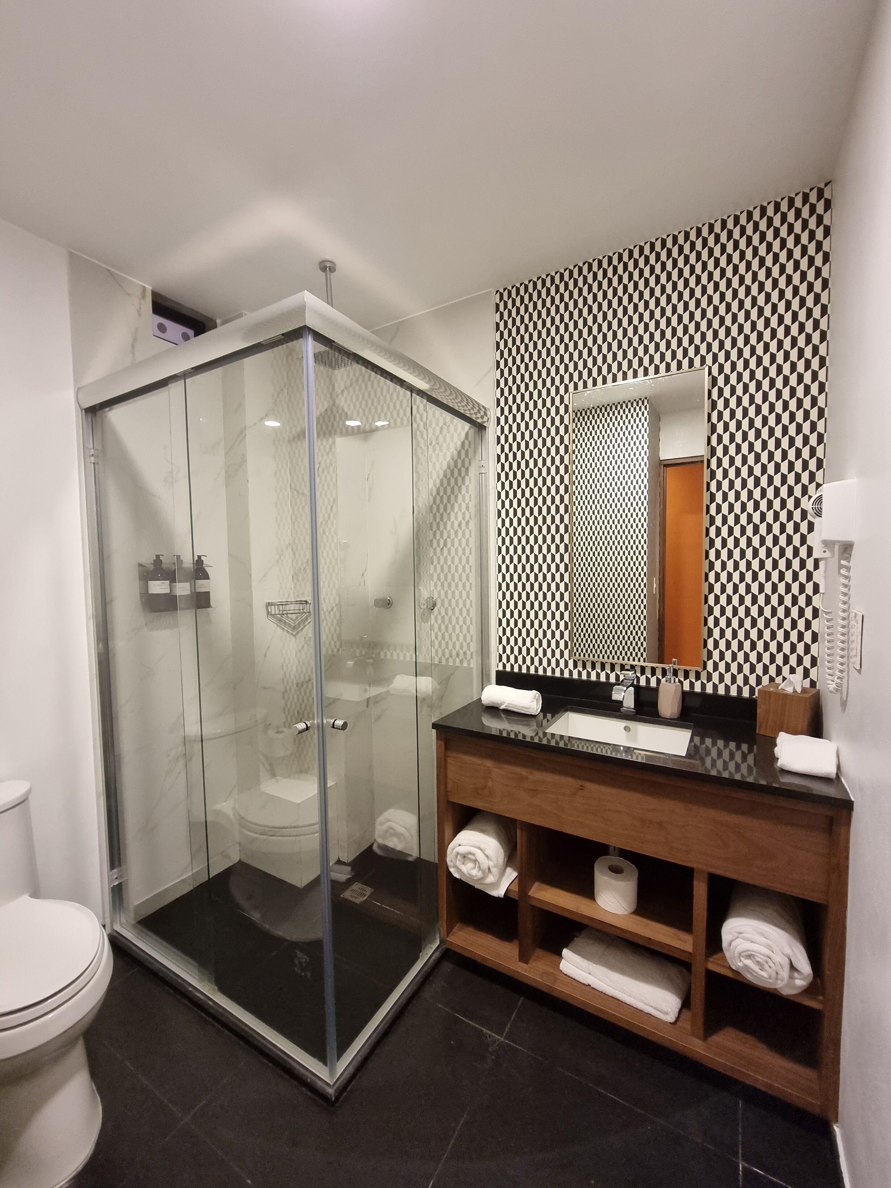 Ein modernes Badezimmer mit einer gläsernen Duschkabine, einem Holzwaschtisch mit schwarzer Arbeitsplatte und einer Wand mit Musterung über dem Spiegel.