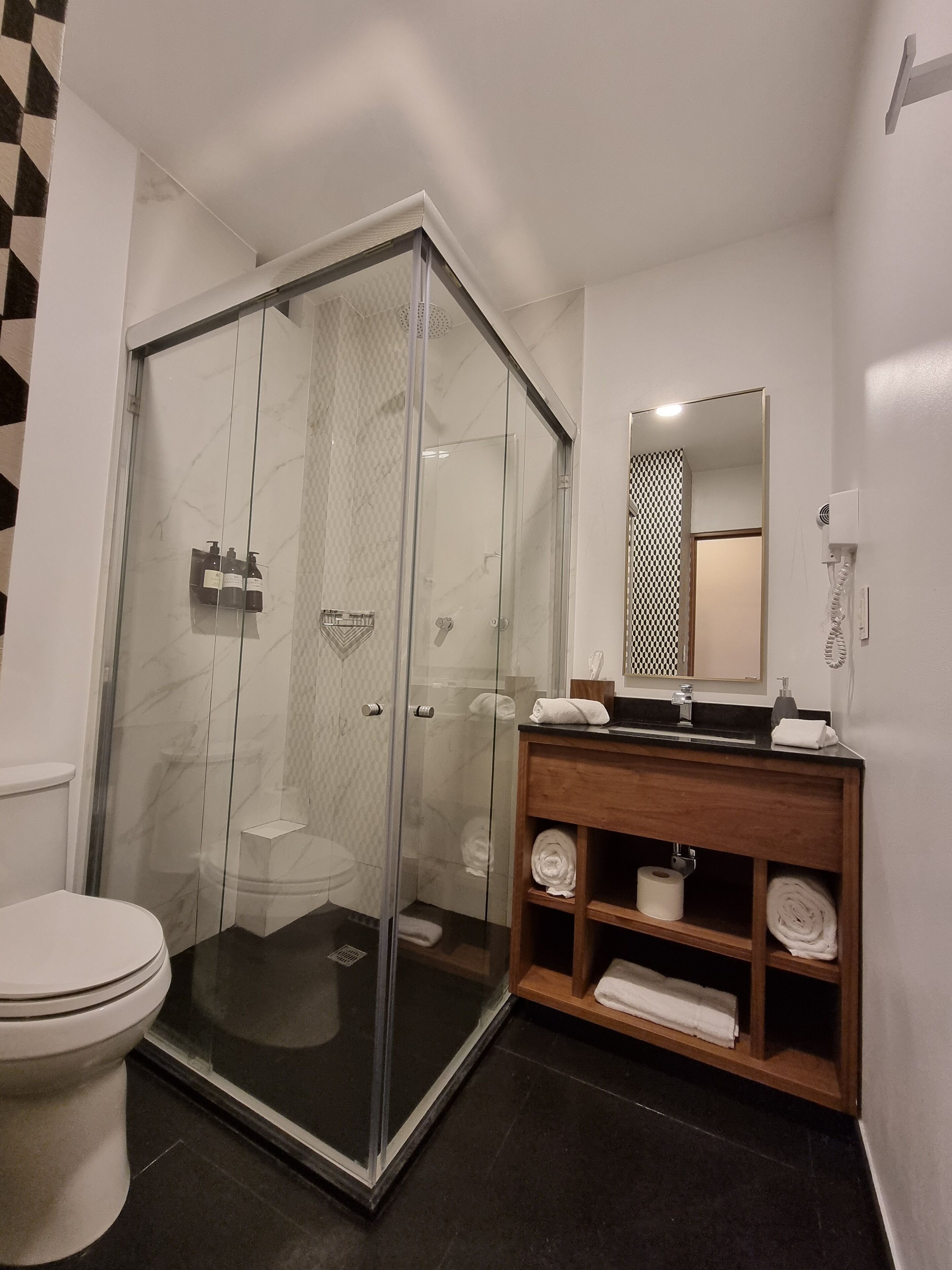 Un baño moderno con ducha de vidrio, tocador de madera con espejo y un inodoro.