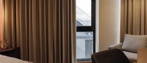A hotel room with a bed, a chair, a sofa, and a large window with curtains.