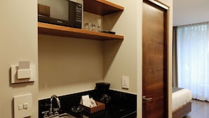 Une chambre d’hôtel compacte dotée d’une kitchenette, d’un four à micro-ondes, d’une machine à café et d’un lit situé près d’une fenêtre.