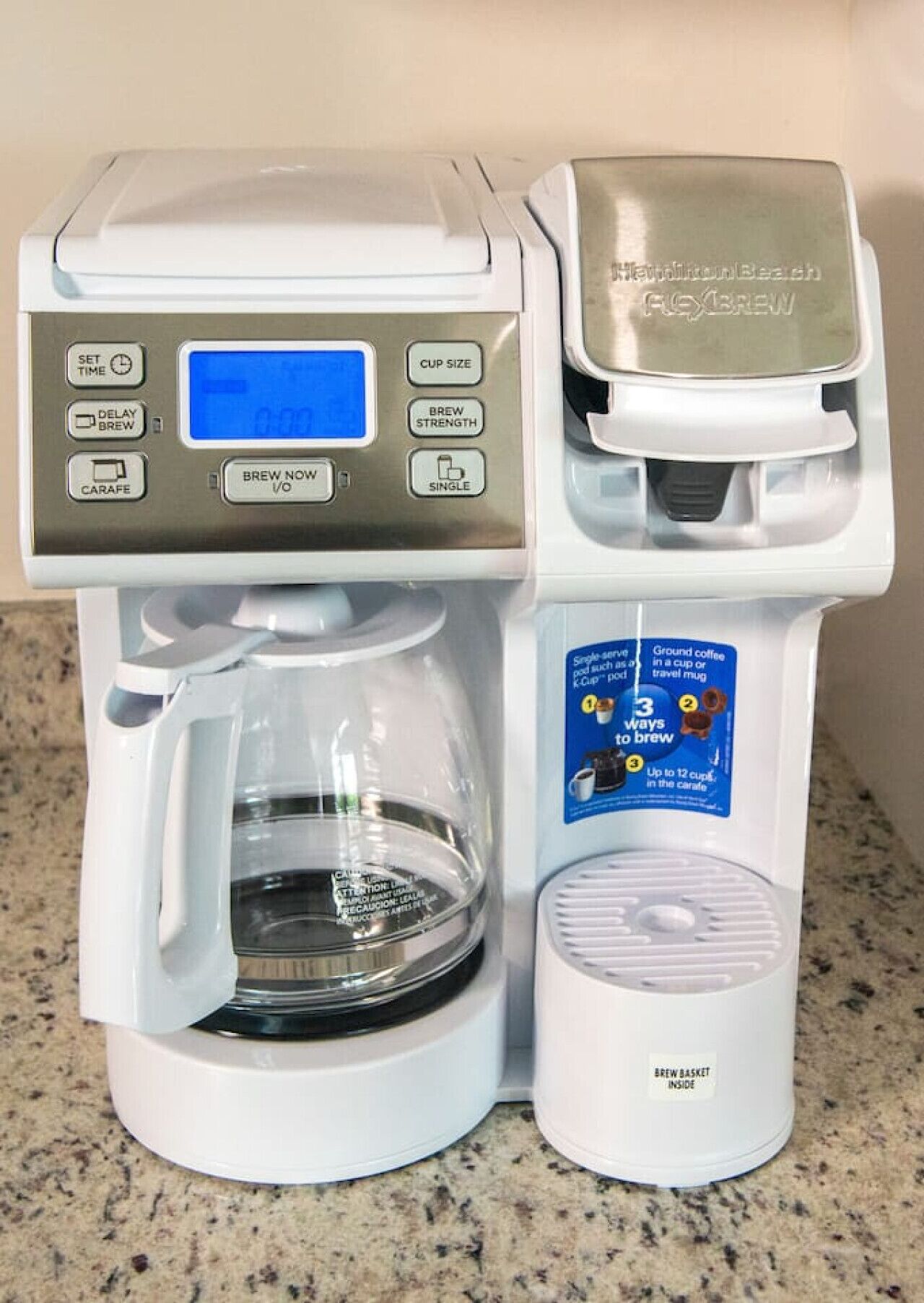A coffee maker with a digital display, a carafe, and a single cup holder.