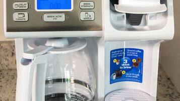 A coffee maker with a digital display, a carafe, and a single cup holder.
