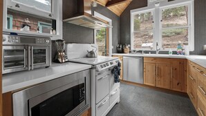 Eine moderne Küche mit Edelstahlgeräten, Holzschränken und großen Fenstern mit Blick ins Freie.