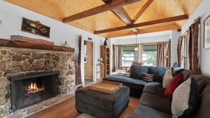 Ein gemütliches Wohnzimmer mit Kamin aus Stein, einem dunkelgrauen Ecksofa und Holzbalken an der Decke.