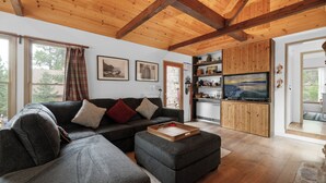 Ein modernes Wohnzimmer mit einer Eckcouch, einer Holz-Unterhaltungsecke und einem großen Fenster mit Vorhängen.