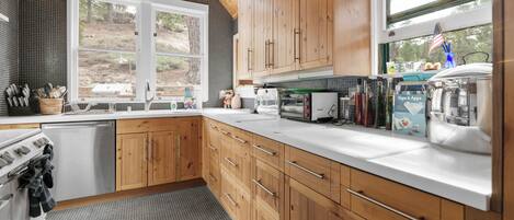 A modern kitchen with wooden cabinets, a stainless steel dishwasher, and a large window providing a view of the outdoors.