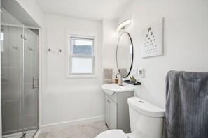 Un bagno moderno con box doccia in vetro, lavandino bianco, WC e finestra che permette l'ingresso di luce naturale.