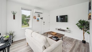 A modern living room with a white sofa, a coffee table, and a TV mounted on the wall. - 15 min. to Detroit center - bathroom with floor heating - free curbside parking (River Rouge)