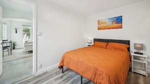 A bedroom with a bed, two bedside tables, a nightstand, a painting, and a view into the adjacent living area. - 15 min. to Detroit center - bathroom with floor heating - free curbside parking (River Rouge)