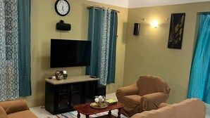 Una sala de estar con un sofá, un televisor de pantalla plana, un reloj y un tapete estampado.