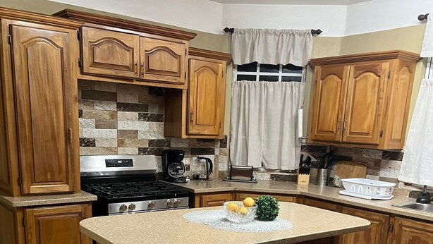 Una cocina con armarios de madera, una isla central con taburetes, una estufa y una cafetera.