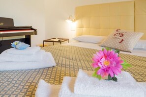 Habitació d'hotel amb un llit, un piano i una tauleta de nit amb una làmpada.