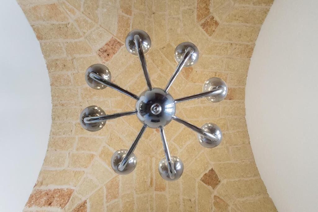 A ceiling with a central metallic fixture and eight surrounding spherical elements, set against a stone wall.