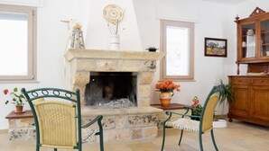 A cozy living room with a stone fireplace, two wicker chairs, a wooden cabinet, and a potted plant. - Aunts' Garden - Sun Room (TRICASE (LE))