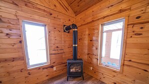 Une cabane avec un poêle à bois, deux fenêtres et des murs en bois.