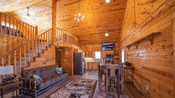 A log cabin interior with a staircase, a living area with a sofa and rug, a kitchen area, and a mounted television. - Amazing Lake of the Woods 2-bedroom cabin with loft and man cave in Baudette, MN (Williams)