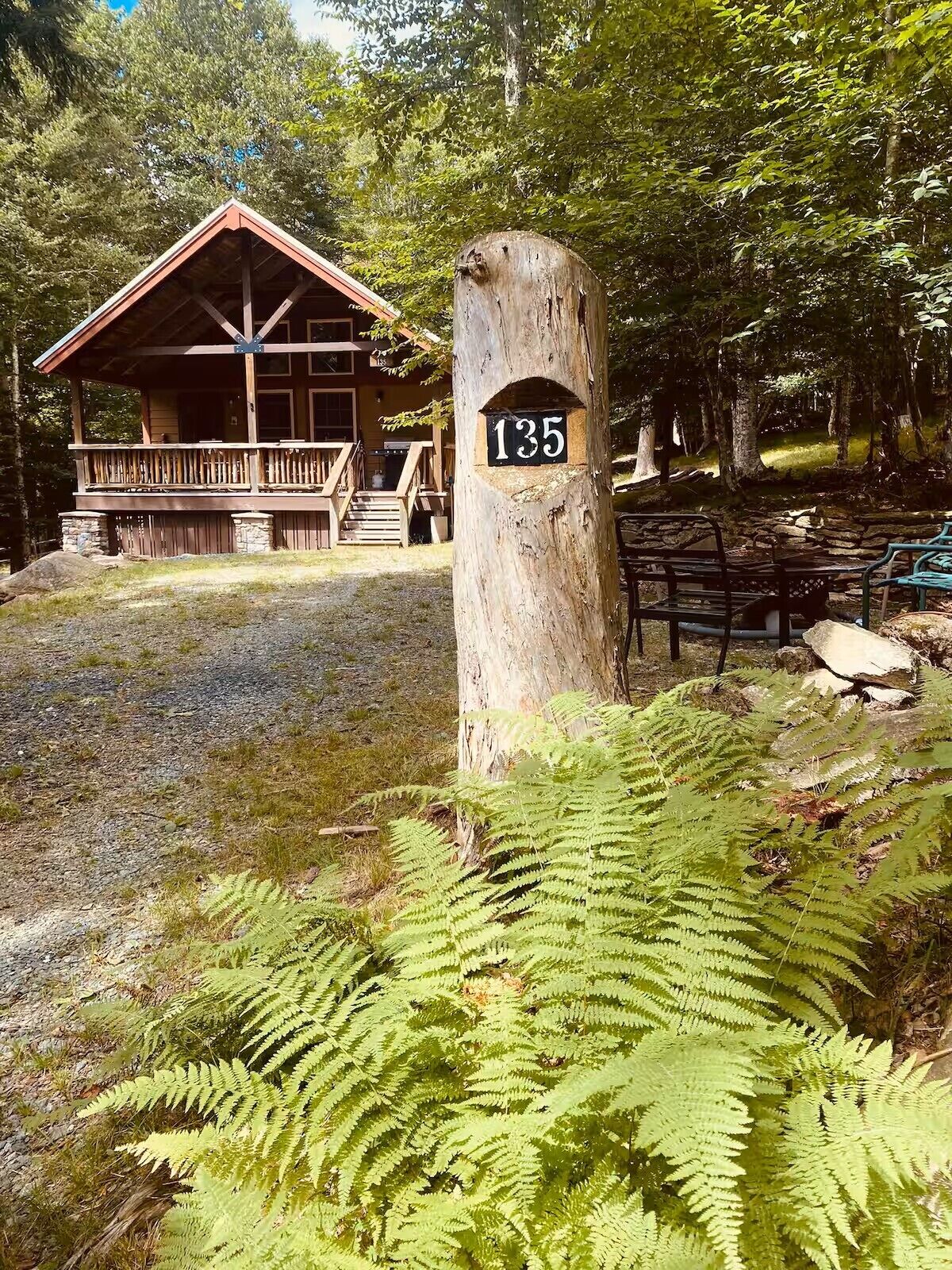Eine Lodge mit einer Holzterrasse und einer blockhaushalähnlichen Struktur. Im Vordergrund steht ein Baum mit einem Schild, das die Nummer 135 zeigt.