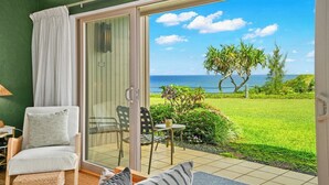 A room with a sliding glass door leading to a balcony with a view of the ocean and a garden.