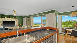 A modern kitchen with a large island, a dining area with a view, and a living room with a TV.