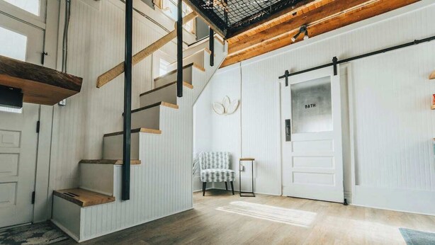 A spacious room with a wooden staircase, a white door labeled "BATH," and a chair. - The Banana Hammock (Logan)