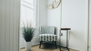 A corner room with a patterned chair, a potted plant, a floor lamp, and a white door. - The Banana Hammock (Logan)