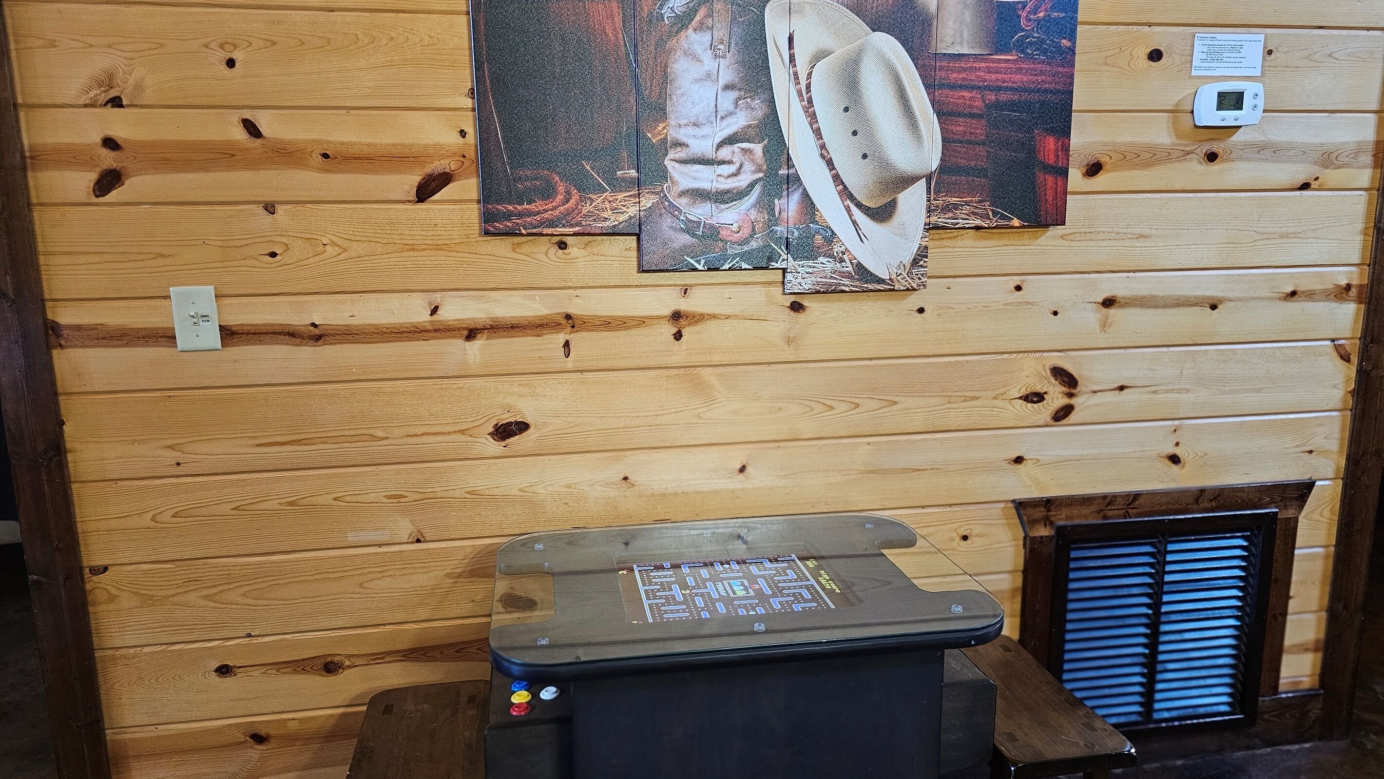 A wooden cabin interior with a mounted heater, a wall-mounted thermostat, and a rustic painting.