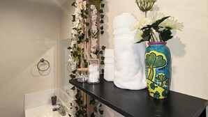 A bathroom with a black shelf holding a vase with flowers, a toilet paper holder, and a towel rack. - Serene studio (Tampa)