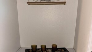 A white shelf with a decorative metal frame holding a framed picture, three candle holders, and a black box. Below, there are two grey storage bins and a wicker basket. - Serene studio (Tampa)
