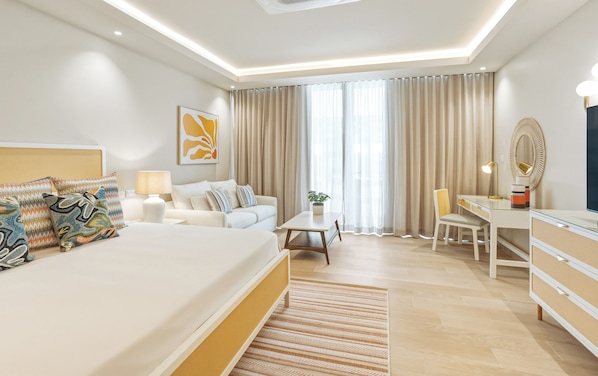 A modern hotel room with a large bed, a desk, a chair, a lamp, and a potted plant.