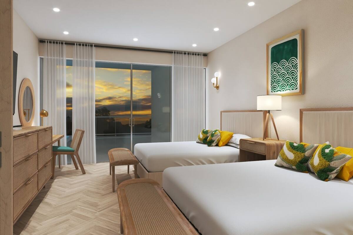 A hotel room with two beds, a desk, a chair, and a view of the sunset through large windows.