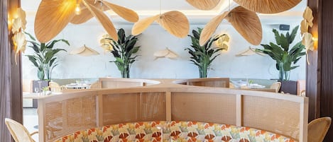 Une table de salle à manger ronde, accompagnée d’un banc en osier tressé, le tout entouré de chaises en rotin.