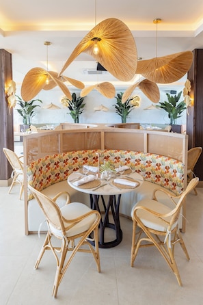 A round dining table with a woven bench, surrounded by wicker chairs.