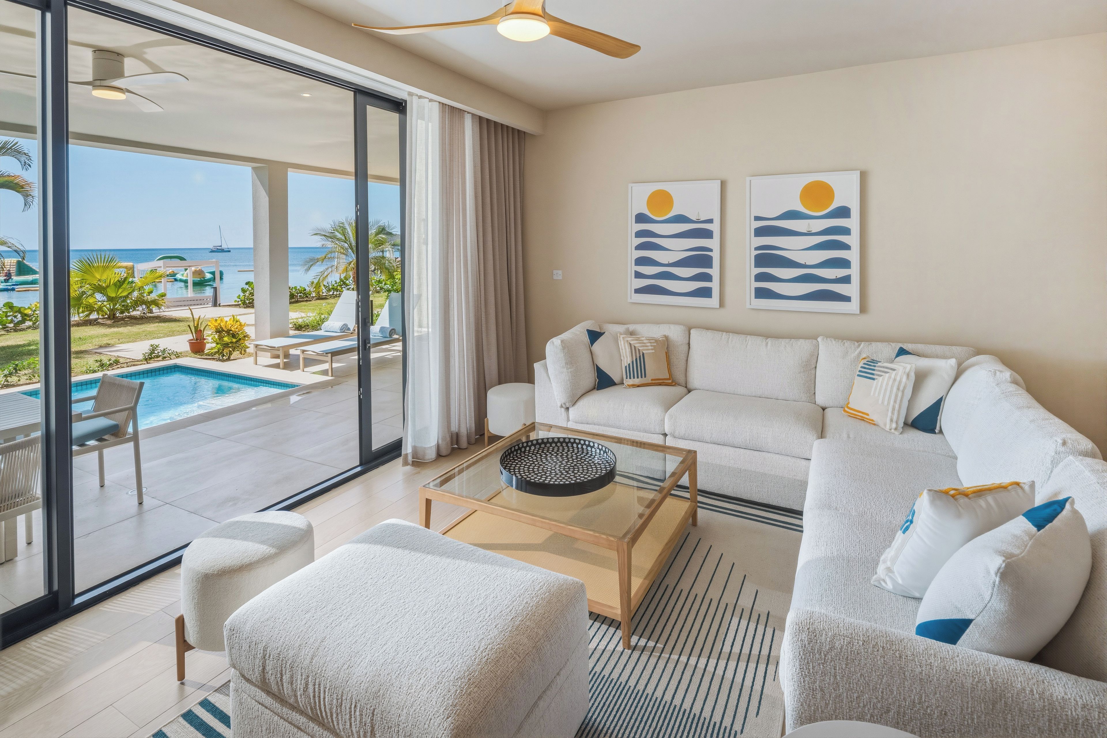 Ein modernes Wohnzimmer mit einem Glastisch, einer Couch und Blick auf ein Schwimmbad und den Ozean.