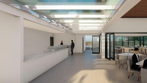 Un moderno vestíbulo de hotel con techo de cristal, un mostrador de recepción y un área de comedor con mesas y sillas.