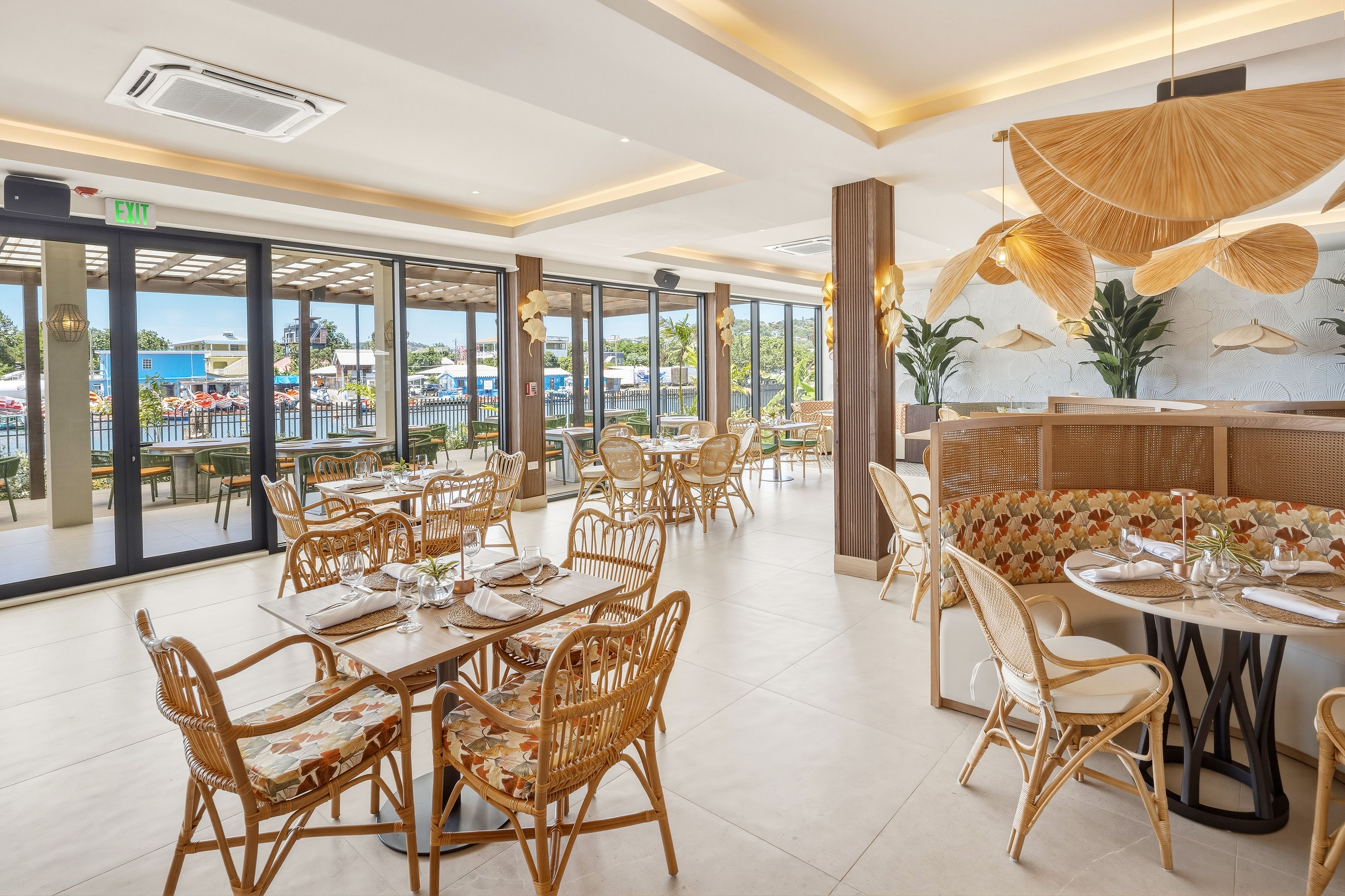Ein Restaurant mit Korbmöbeln, großen Fenstern und Blick aufs Meer.