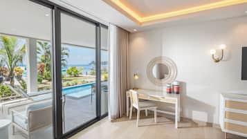 Quarto de hotel moderno com uma grande porta de correr de vidro que dá para uma área de piscina, uma escrivaninha com cadeira, um espelho redondo e um pequeno armário.