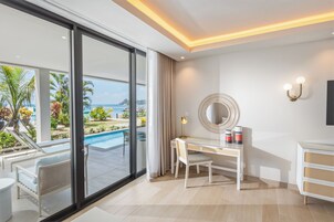 Een moderne hotelkamer met een grote schuifglazen deur die uitkomt op een zwembad, een bureau met stoel, een ronde spiegel en een klein kastje.
