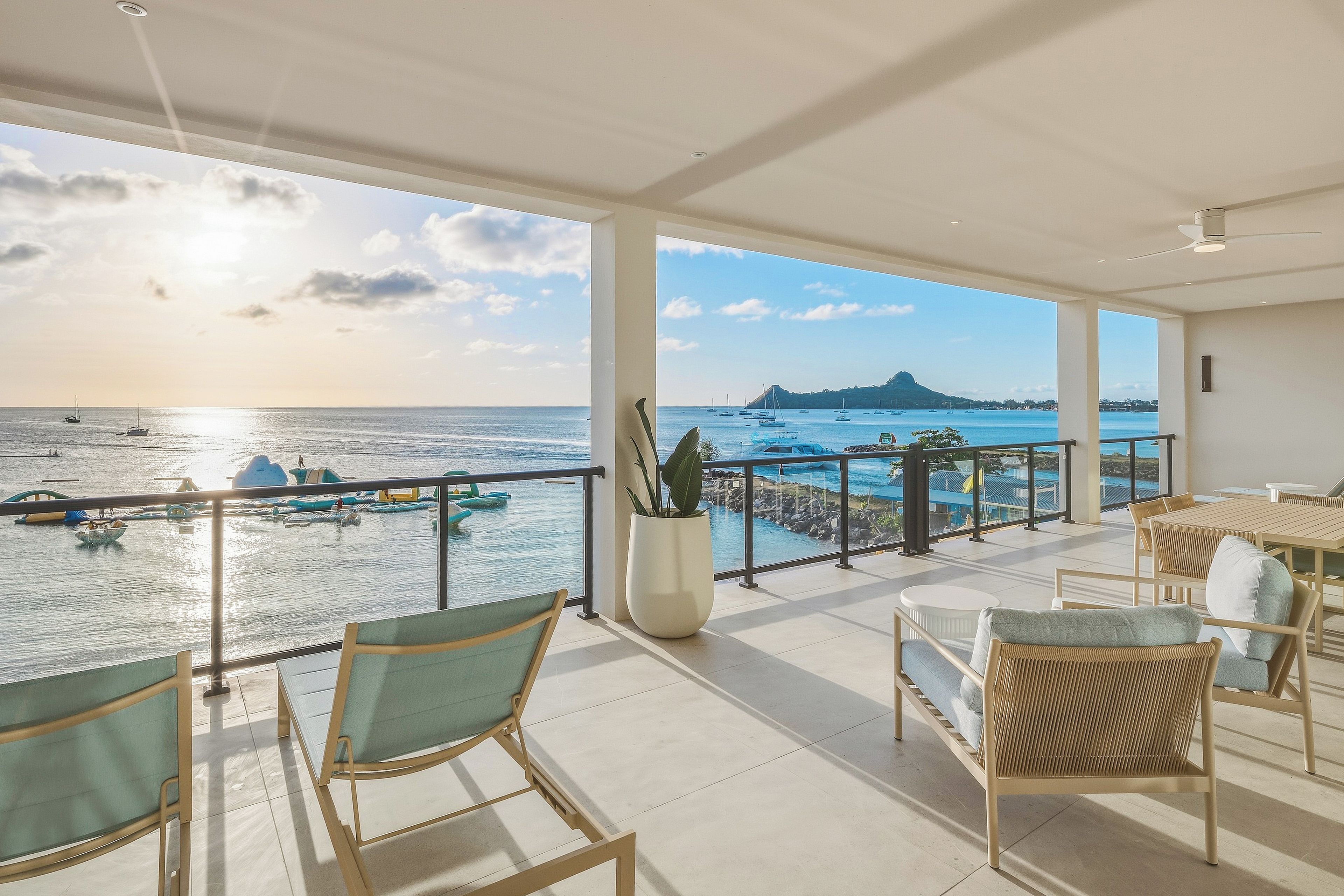 Uma varanda com vista para o mar, com cadeiras de descanso e um vaso de plantas.