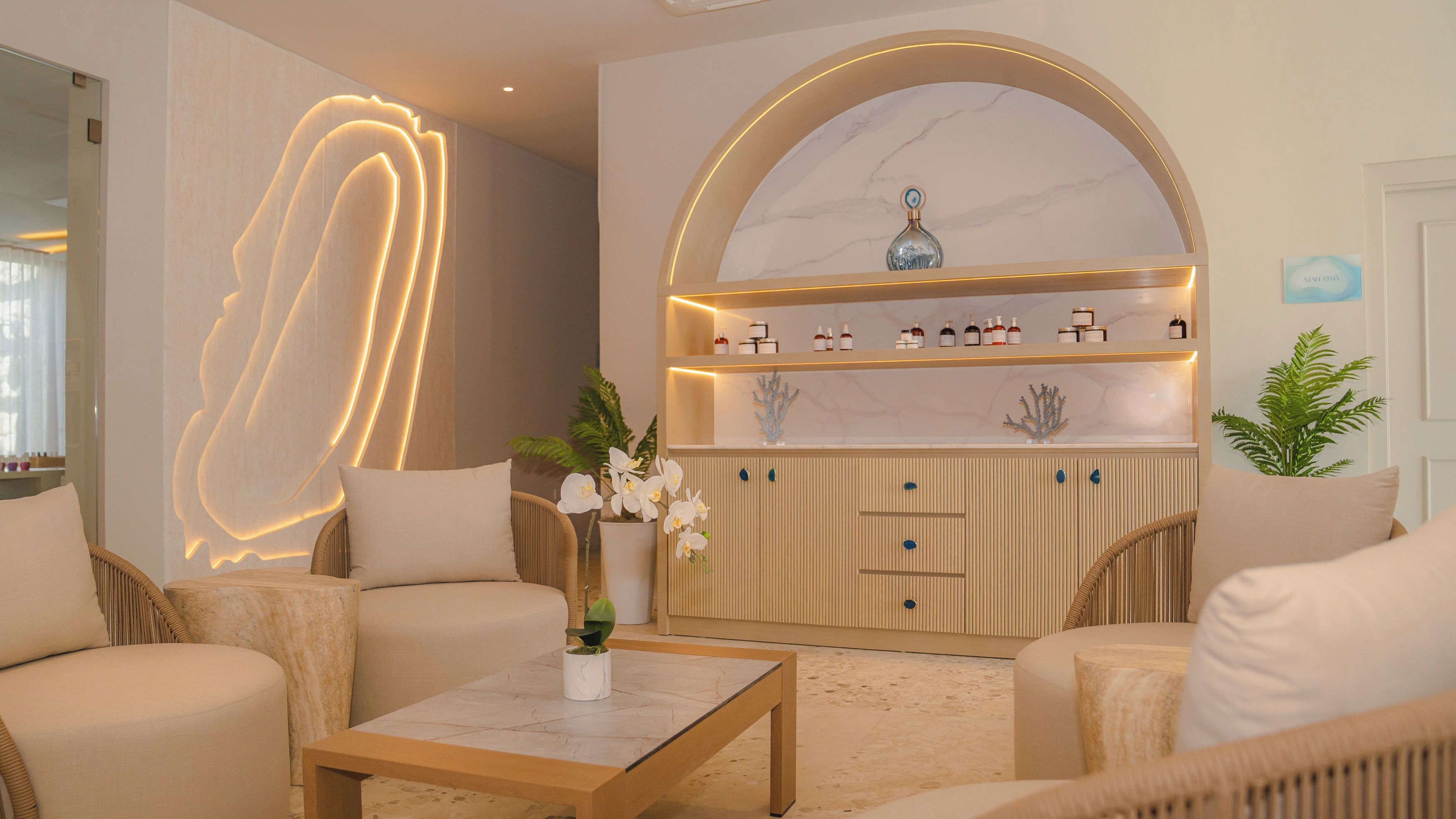 Un interior moderno con una zona de estar, una encimera de mármol con botellas y una pared con un diseño de iluminación.