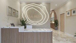 A reception area with a marble counter, a large illuminated 'LA MER' sign, framed artwork on the walls, and potted plants.
