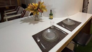 A modern kitchen with a long countertop, two clear glass plates, a bottle of wine, and a vase with dried flowers. - Studio- Spacious garden area / on-site car rental (Saint John's)