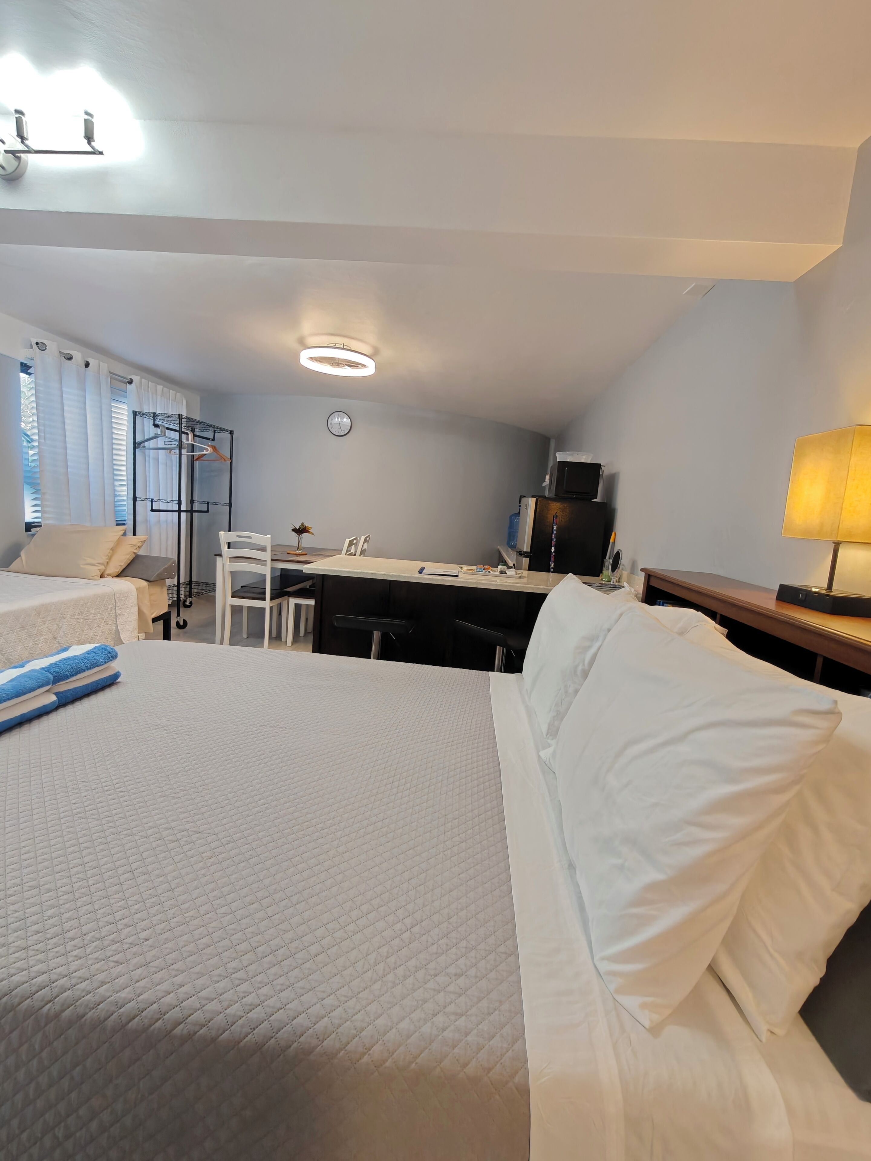 A hotel room with two beds, a desk, a chair, a clock, and a lamp.