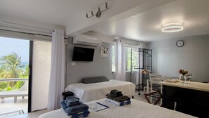Habitación de hotel con una cama grande, un escritorio, una silla, un televisor y un balcón con vistas a palmeras.