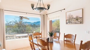 A dining area with a large round table, six wooden chairs, a chandelier, and a view of a desert landscape through large windows. - Charming 3-bedroom house with AC, WiFi in tranquil Cottonwood (Cottonwood)