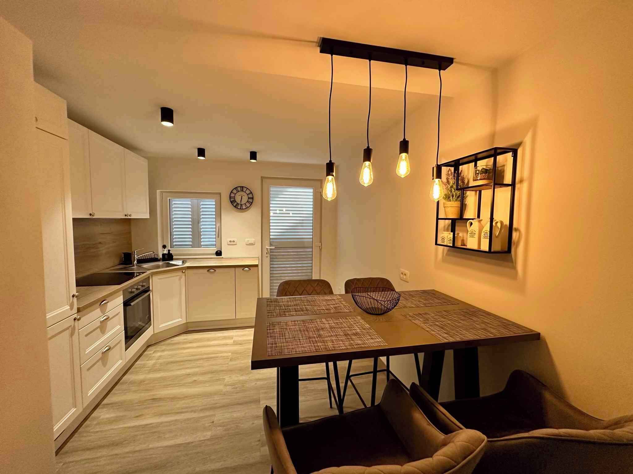 A compact kitchen with modern appliances, a dining area with a wooden table and chairs, and a wall-mounted shelf with decorative items.