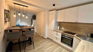 A modern kitchen with a wooden countertop, built-in oven, and a sink. There are two bar stools and a dining table with hanging pendant lights. - Holiday home with air conditioning (Jadranovo)