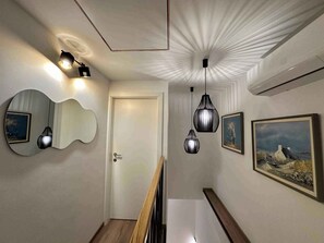 A hallway with a wooden floor, a white door, a wall-mounted mirror, and three hanging pendant lights.