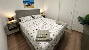 A neatly made bed with a patterned bedspread, two bedside tables with lamps, a painting on the wall, and a door to the right. - Holiday home with air conditioning (Jadranovo)