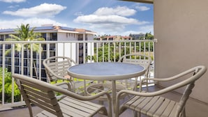 Een balkon met een ronde tafel en vier stoelen, met uitzicht op een woongebied met gebouwen en palmbomen.
