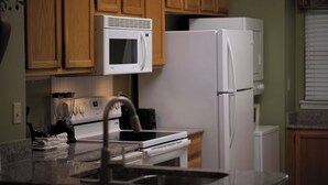 A kitchen with wooden cabinets, a white microwave, a white refrigerator, a sink, and a countertop with a blender and towels.